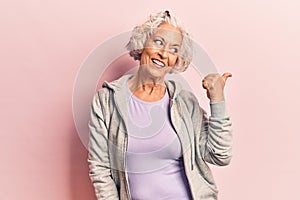 Senior grey-haired woman wearing casual sporty clothes smiling with happy face looking and pointing to the side with thumb up