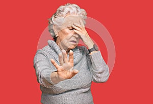 Senior grey-haired woman wearing casual winter sweater covering eyes with hands and doing stop gesture with sad and fear