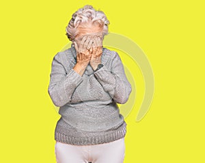 Senior grey-haired woman wearing casual winter sweater with sad expression covering face with hands while crying