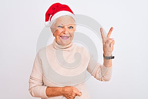 Senior grey-haired woman wearing Crhistmas Santa hat over isolated white background smiling with happy face winking at the camera