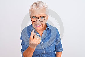 Senior grey-haired woman wearing denim shirt and glasses over isolated white background Beckoning come here gesture with hand