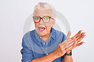 Senior grey-haired woman wearing denim shirt and glasses over isolated white background clapping and applauding happy and joyful,