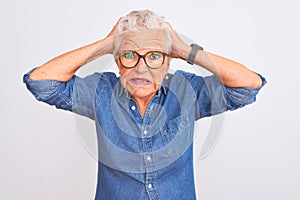 Senior grey-haired woman wearing denim shirt and glasses over isolated white background Crazy and scared with hands on head,