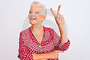 Senior grey-haired woman wearing red casual jacket standing over isolated white background smiling with happy face winking at the