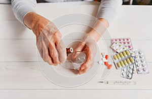 Senior hands with medicine bottle putting drops in a glass, pills, drugs, thermometer on a table.