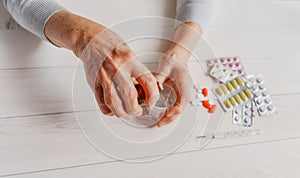 Senior hands with medicine bottle putting drops in a glass, pills, drugs, thermometer on a table.