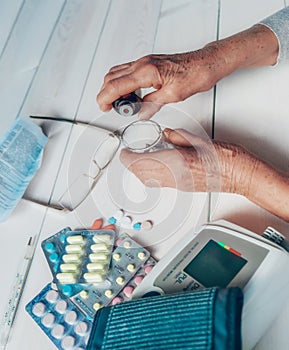 Senior hands with medicine bottle putting drops in a glass, pills, tonometer, thermometer on a table.