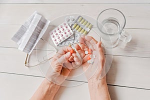 Senior hands with pills and drugs on table, glass of water.
