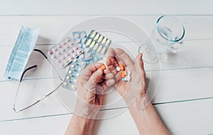 Senior hands with pills and drugs on table, glass of water.