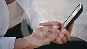 Senior hands touching cellphone screen browsing internet on street close up.