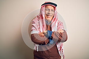 Senior handsome arab man wearing keffiyeh standing over isolated white background happy face smiling with crossed arms looking at