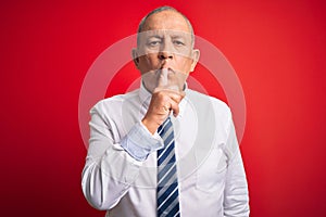 Senior handsome businessman wearing elegant tie standing over isolated red background asking to be quiet with finger on lips