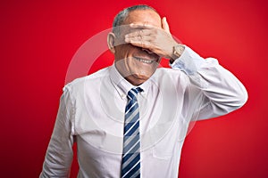 Senior handsome businessman wearing elegant tie standing over isolated red background smiling and laughing with hand on face