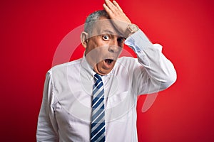 Senior handsome businessman wearing elegant tie standing over isolated red background surprised with hand on head for mistake,