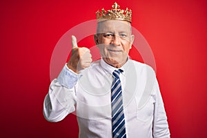 Senior handsome businessman wearing king crown standing over isolated red background doing happy thumbs up gesture with hand