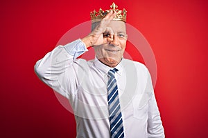 Senior handsome businessman wearing king crown standing over isolated red background doing ok gesture with hand smiling, eye
