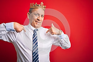 Senior handsome businessman wearing king crown standing over isolated red background looking confident with smile on face,