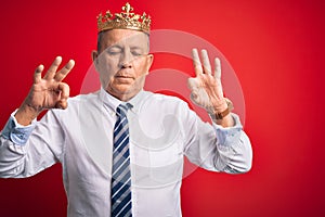 Senior handsome businessman wearing king crown standing over isolated red background relax and smiling with eyes closed doing