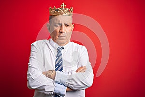 Senior handsome businessman wearing king crown standing over isolated red background skeptic and nervous, disapproving expression