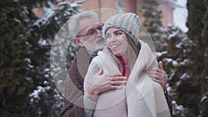 Senior handsome Caucasian man covering young woman with blanket. Portrait of happy couple with age difference enjoying