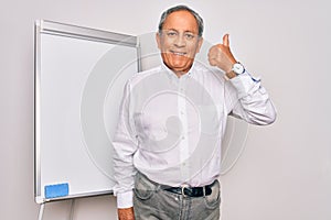 Senior handsome grey-haired businessman doing presentation using magnetic board doing happy thumbs up gesture with hand