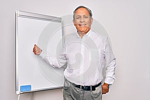 Senior handsome grey-haired businessman doing presentation using magnetic board smiling with happy face looking and pointing to