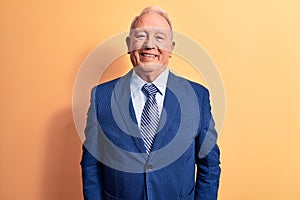 Senior handsome grey-haired businessman wearing elegant suit over yellow background with a happy and cool smile on face