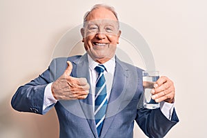 Senior handsome grey-haired businessman wearing suit drinking glass of water to refreshment smiling happy and positive, thumb up
