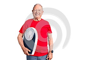 Senior handsome grey-haired man holding weighing machine looking positive and happy standing and smiling with a confident smile