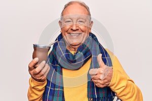 Senior handsome grey-haired man wearing casual scarf drinking cup of mate infusion beverage smiling happy and positive, thumb up