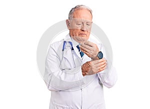 Senior handsome grey-haired man wearing doctor coat and stethoscope suffering pain on hands and fingers, arthritis inflammation