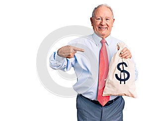 Senior handsome grey-haired man wearing elegant clothes holding money bag pointing finger to one self smiling happy and proud