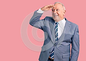 Senior handsome grey-haired man wearing elegant suit very happy and smiling looking far away with hand over head