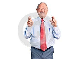 Senior handsome grey-haired man wearing elegant tie and shirt gesturing finger crossed smiling with hope and eyes closed