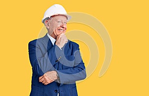 Senior handsome grey-haired man wearing suit and architect hardhat with hand on chin thinking about question, pensive expression