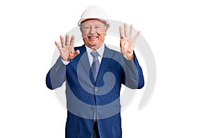 Senior handsome grey-haired man wearing suit and architect hardhat showing and pointing up with fingers number nine while smiling