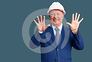 Senior handsome grey-haired man wearing suit and architect hardhat showing and pointing up with fingers number ten while smiling