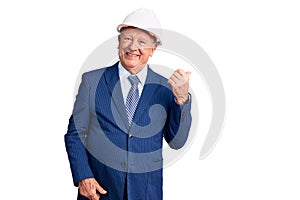 Senior handsome grey-haired man wearing suit and architect hardhat smiling with happy face looking and pointing to the side with