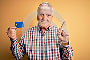 Senior handsome hoary customer man holding credit card to finance payment surprised with an idea or question pointing finger with