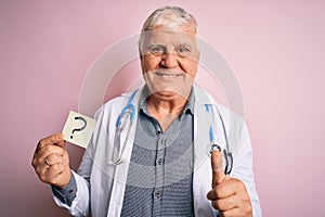 Senior handsome hoary doctor man wearing stethoscope holding reminder with question mark happy with big smile doing ok sign, thumb