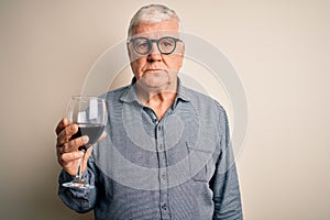 Senior handsome hoary man drinking glass of red wine over isolated white background with a confident expression on smart face
