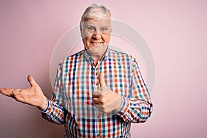 Senior handsome hoary man wearing casual colorful shirt over isolated pink background Showing palm hand and doing ok gesture with