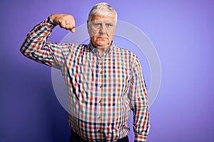 Senior handsome hoary man wearing casual colorful shirt over isolated purple background Strong person showing arm muscle,