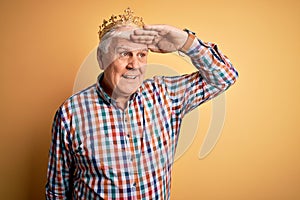 Senior handsome hoary man wearing golden crown of king over isolated yellow background very happy and smiling looking far away