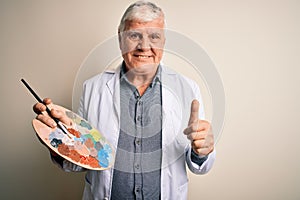 Senior handsome hoary painter man painting using brush and palette with colors happy with big smile doing ok sign, thumb up with