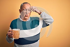 Senior handsome man drinking jar of beer standing over isolated yellow background worried and stressed about a problem with hand