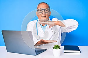 Senior handsome man with gray hair wearing doctor uniform working using computer laptop gesturing with hands showing big and large