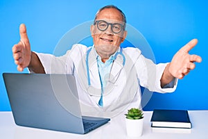 Senior handsome man with gray hair wearing doctor uniform working using computer laptop looking at the camera smiling with open
