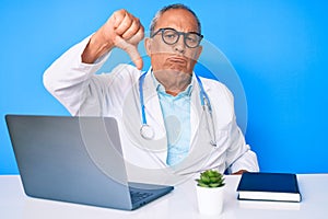 Senior handsome man with gray hair wearing doctor uniform working using computer laptop looking unhappy and angry showing