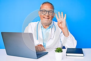 Senior handsome man with gray hair wearing doctor uniform working using computer laptop showing and pointing up with fingers